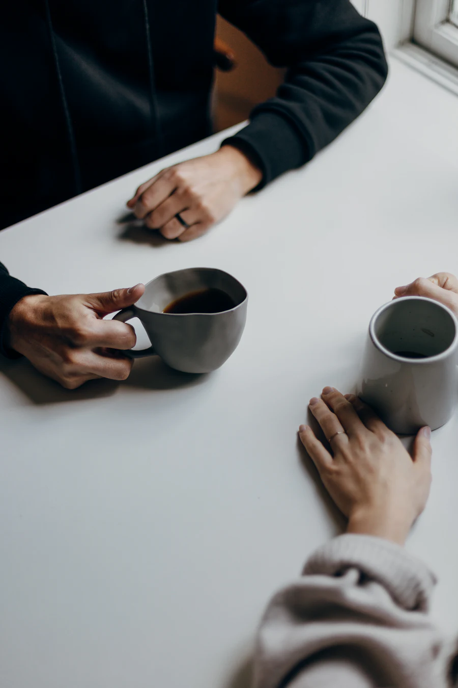 Two people talking across a white table, coffee cups in hand