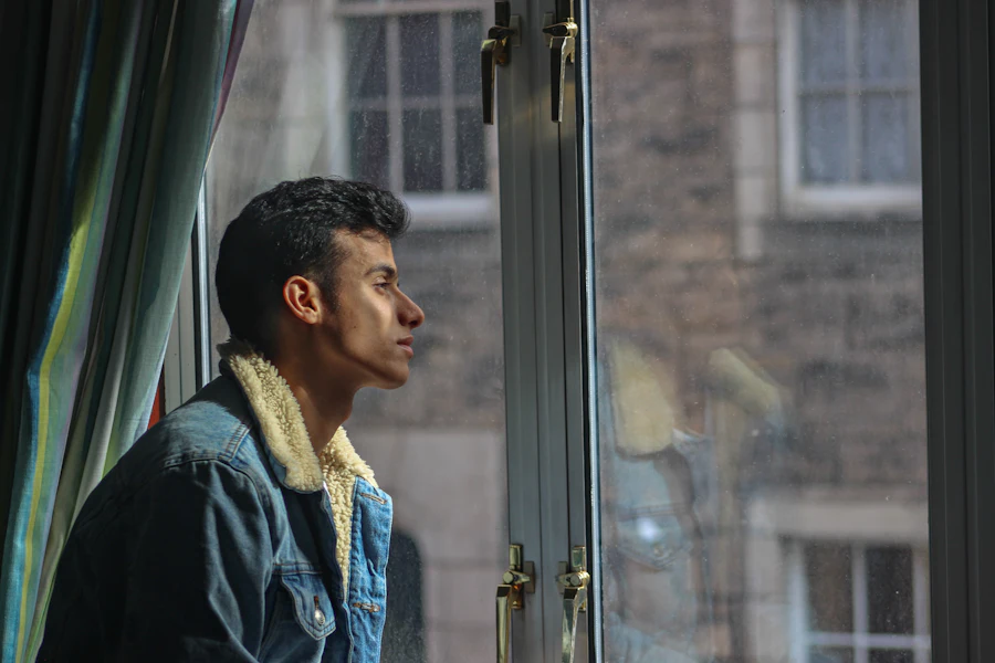 A man in a dark jacket looking out of a window, deep in thought